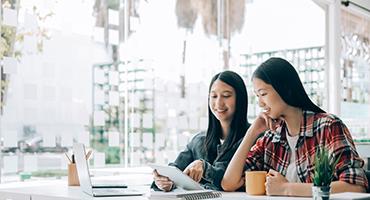 Two students at desk smiling at tablet