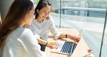 Two students sitting and looking at a laptop together smiling