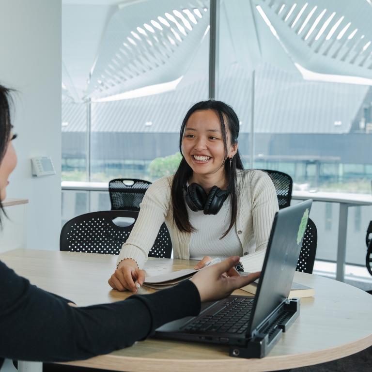 Students sitting at desk over a computer and smiling at each other